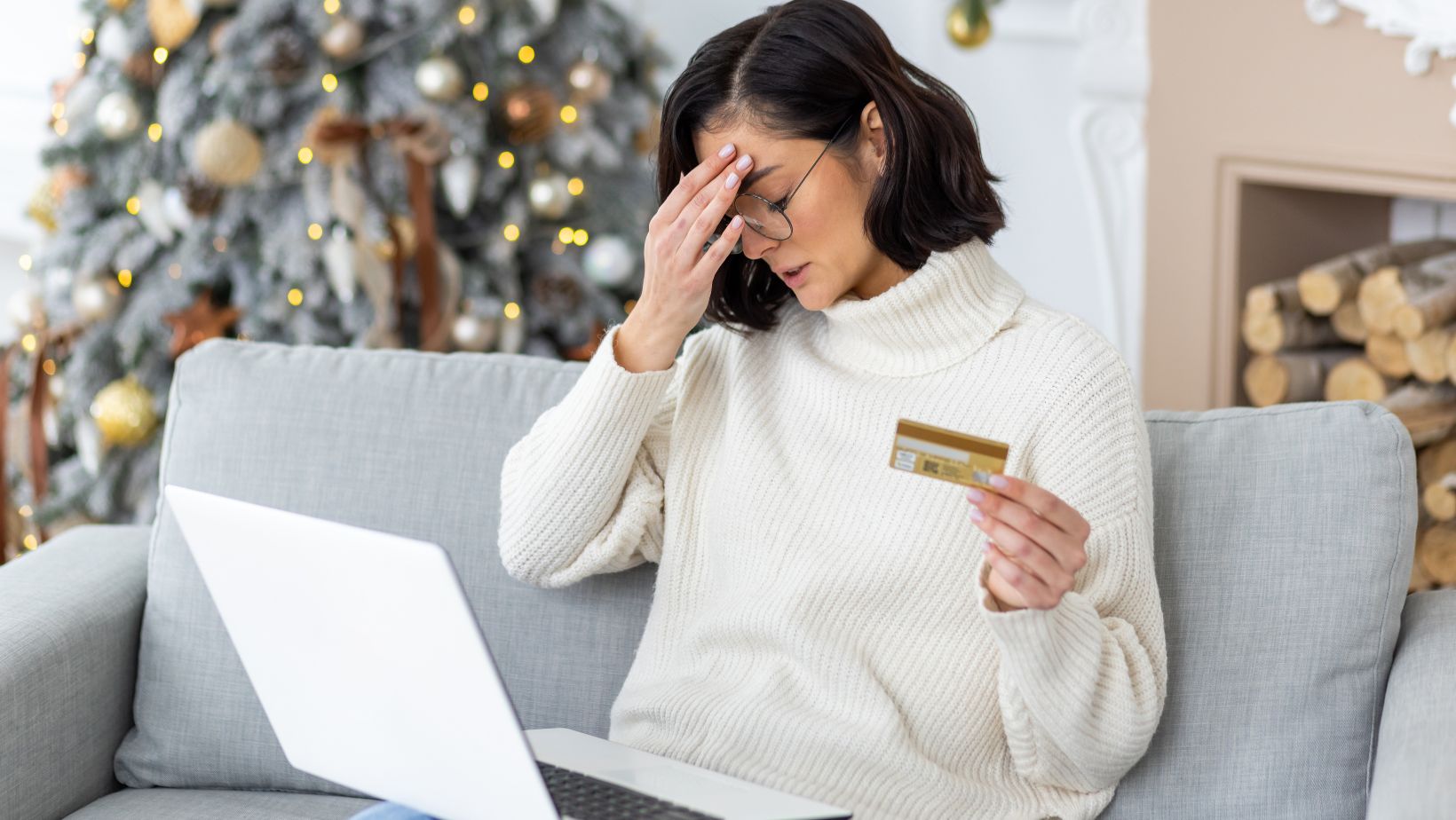 A woman on a sofa with a laptop and credit card, looking frustrated